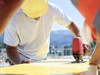 Construction worker cutting plywood with jigsaw on construction site