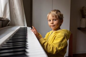 Child, blond boy, playing piano at home