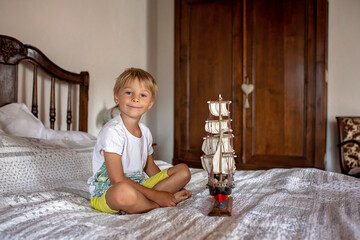 Cute blond child, boy, playing at home with toys, ship, dolls