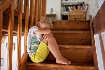Cute blond child, boy, sitting on staircase, sad and lonely
