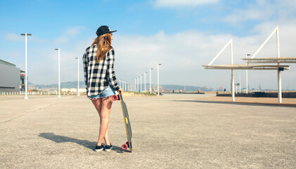 Back view of young woman with longboard standing in front of beach promenade, partial view