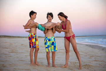 Happy children, boys, playing on the beach on sunset, kid cover in sand, smiling, laughing