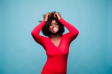 Young woman in studio wearing red dress making a chewing gum bubble
