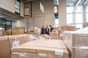 Three men in factory warehouse surrounded by cardboard boxes