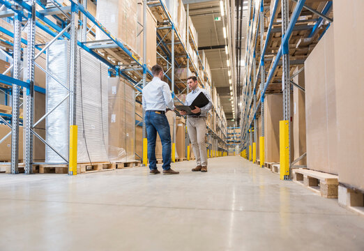 Two men with folder talking in factory warehouse