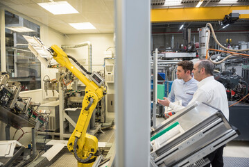 Two men talking in factory shop floor looking at industrial robot