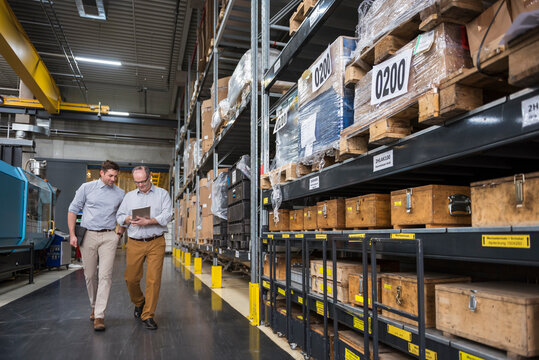 Two men with tablet walking in factory warehouse