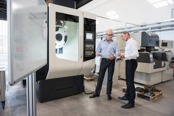 Two men looking at tablet and product in factory