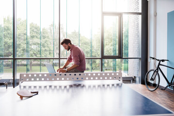 Man using laptop in break room of modern office on table tennis table