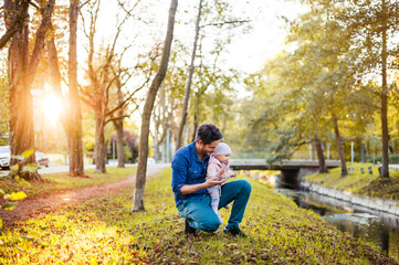 Father searching for chestnuts in park, with baby daughter on his lap