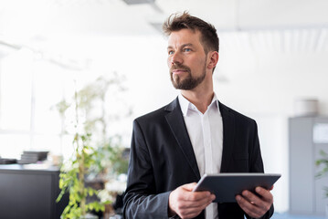 Successful businessman standing in office, using digital tablet