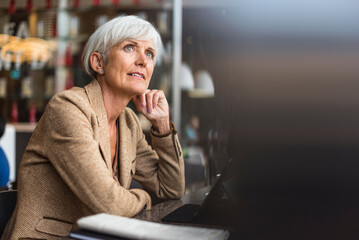 Senior businesswoman with tablet in a cafe thinking