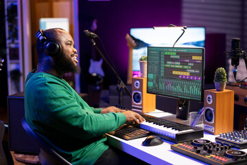 Skilled composer playing piano electronic keyboard to create new music, mixing tunes on digital...