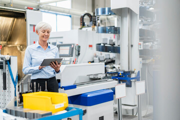 Smiling senior businesswoman using tablet in a factory