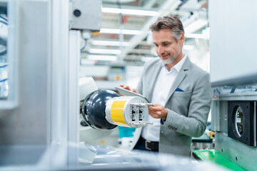 Businessman with tablet at assembly robot in a factory