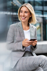 Happy young businesswoman with mobile phone in the city