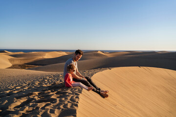 Father and daughter sitting on sand dune, Gran Canaria, Spain