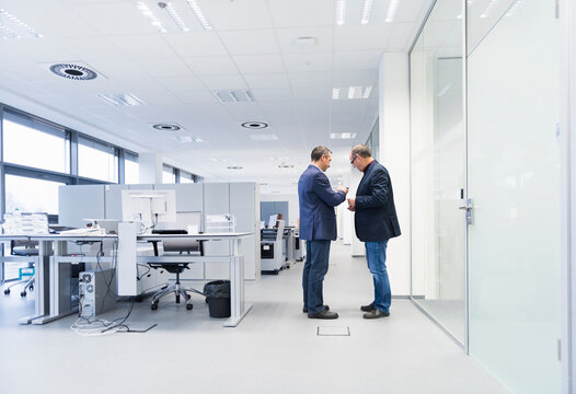 Two businessmen standing in office looking at smartphone