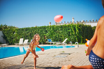 Girl and boy having a water fight with water gun and water bombs at the poolside