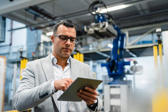 Mature businessman wearing eyeglasses working on digital tablet in industry