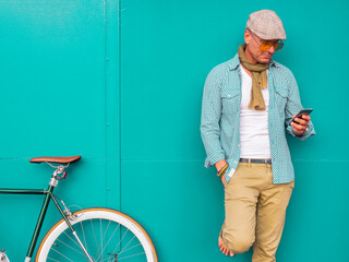 Man with Fixie bike standing in front of green wall looking at cell phone