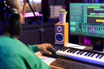 Music engineer adding synthesizer notes over his audio files in home studio, editing tracks with...