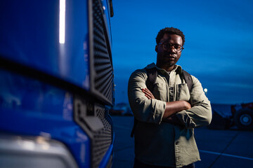 Experienced African American driver standing by his truck ready for night ride.