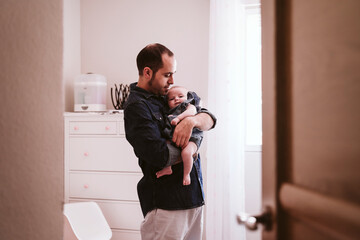 Father carrying cute baby girl in living room at home