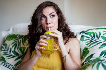 Beautiful young woman with long brown hair sipping juice from straw in mason jar while looking away