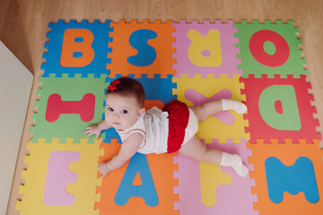 Cute baby girl lying on colorful puzzle playmat at home