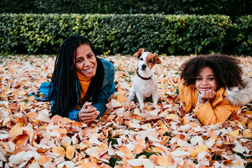 Smiling woman and daughter lying on dry leaf by dog sitting at park