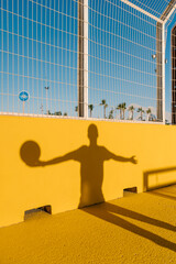 Shadow of young man holding basketball on yellow wall in sports court