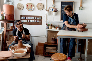 Coworkers talking while making pottery in workshop