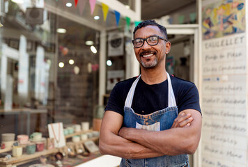 Confident male potter with arms crossed standing outside ceramic shop