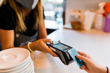 Female cashier receiving payment through credit card from customer in cafe during COVID-19