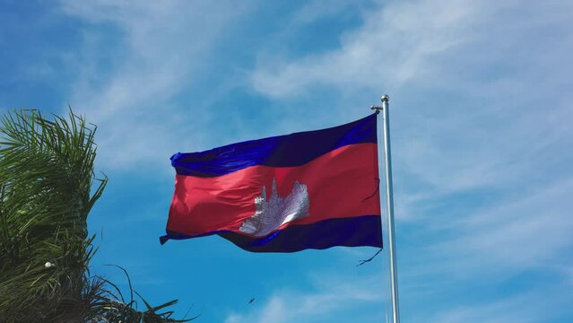 Cambodia's flag waving in the wind, some greenery in frame