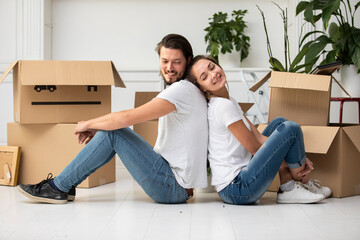 Happy couple with cardboard boxes sitting on the floor in new home