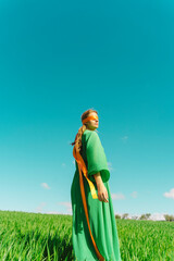 Blindfolded young woman wearing a green dress standing in a field