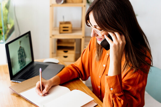 Female fashion designer working at home sitting at desk taking notes