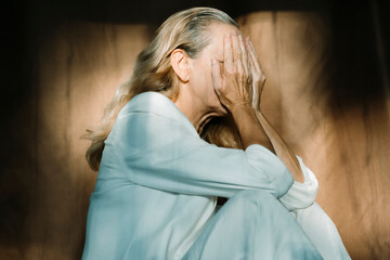 Sad senior woman sitting alone with hands covering face