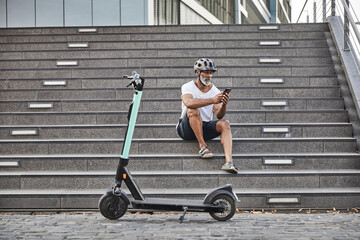 Mature man with E-Scooter sitting on stairs using cell phone