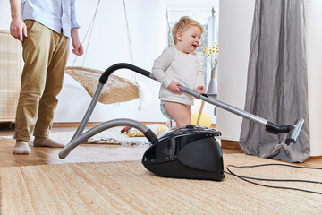 Cute baby boy holding vacuum cleaner while standing on carpet by father at home