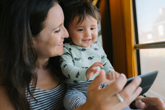 Happy mother and baby girl using smartphone while traveling by train
