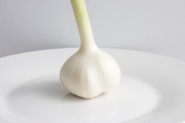 白い皿の上に乗った、茎がついた一個の新ニンニク