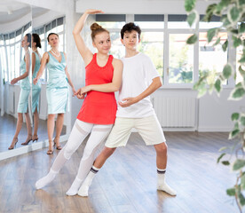 Positive motivated adolescent dance duo, boy and girl, refining slow foxtrot technique in dance...