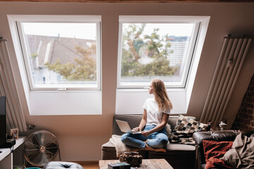 Young woman at home sitting on couch, using laptop