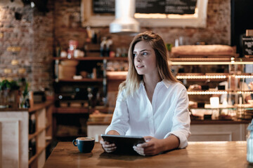 Blond woman sitting in cafe, using tablet, thinking