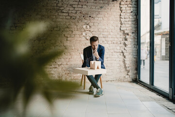 Businessman sitting at brick wall looking at architectural model