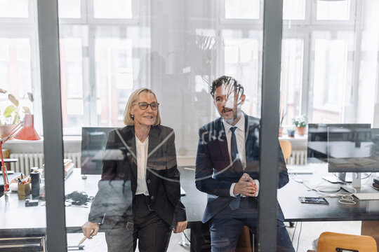 Businessman and businesswoman looking at drawing on glass pane in office