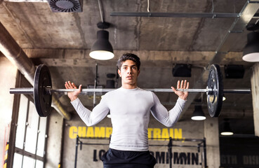 Young athlete lifting barbell in gym